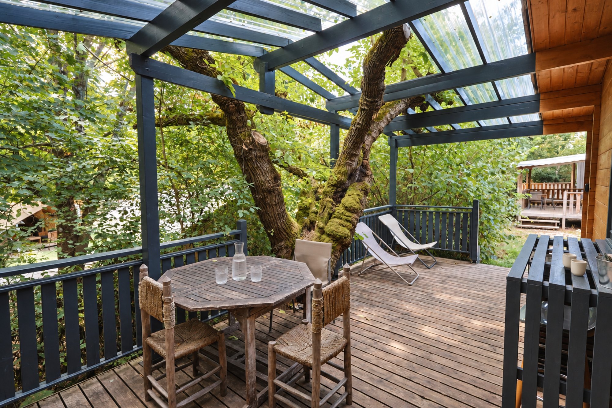 Terrasse du chalet avec table et transats à l’ombre des arbres